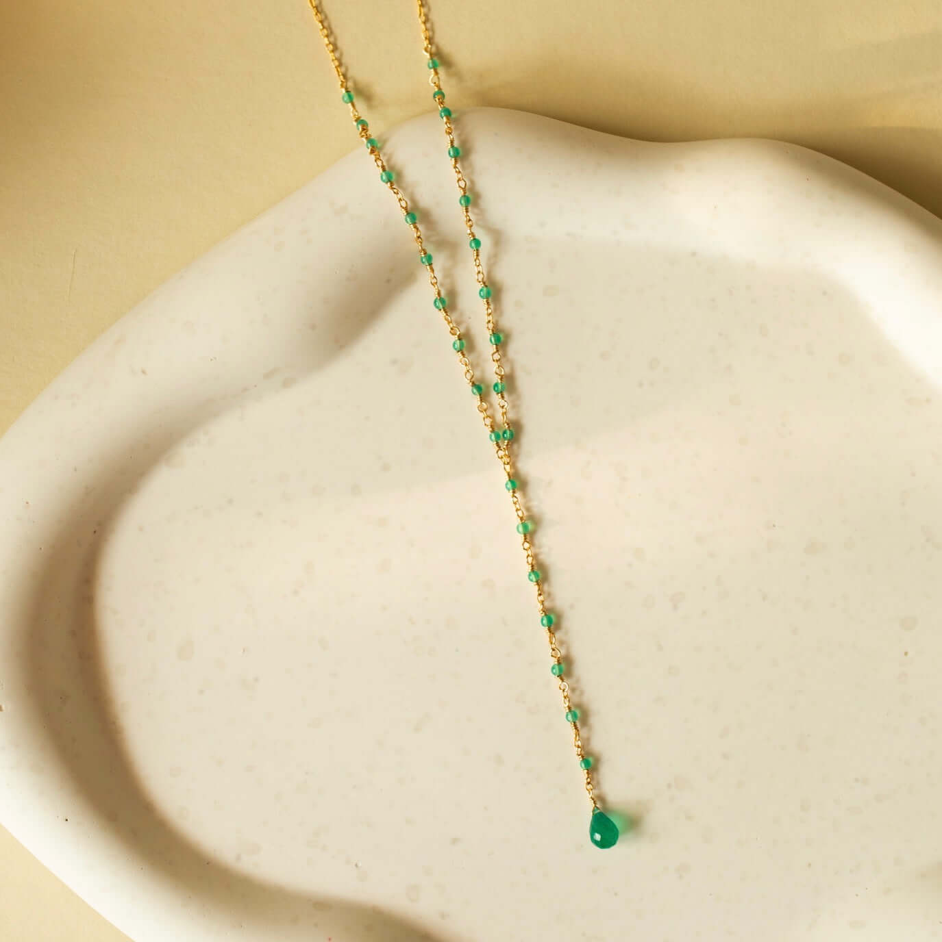 A green onyx necklace rests gracefully on a clay plate, showcasing its vibrant and soothing green hues.