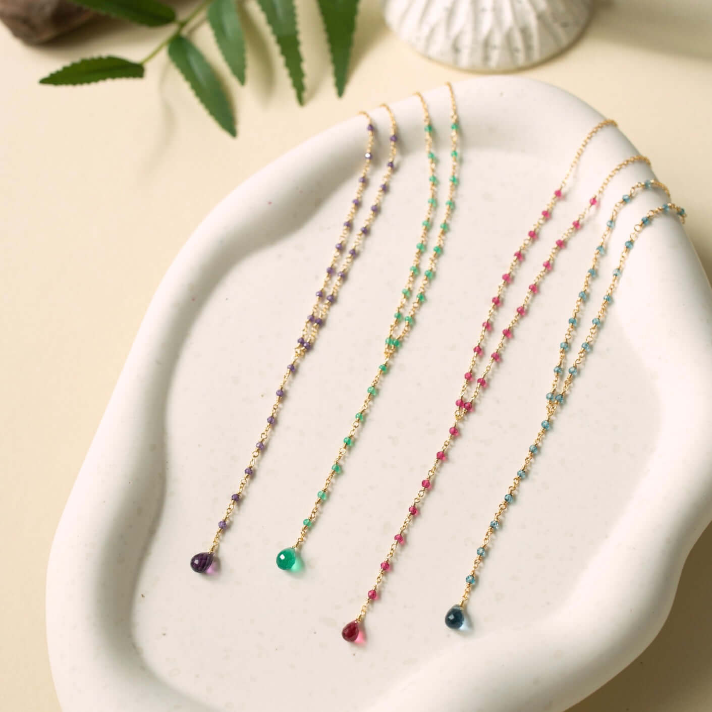 Against a rustic clay plate backdrop, lolite, amethyst, pink tourmaline quartz, and green onyx necklaces unveil their distinct beauty in a charming display of natural elegance