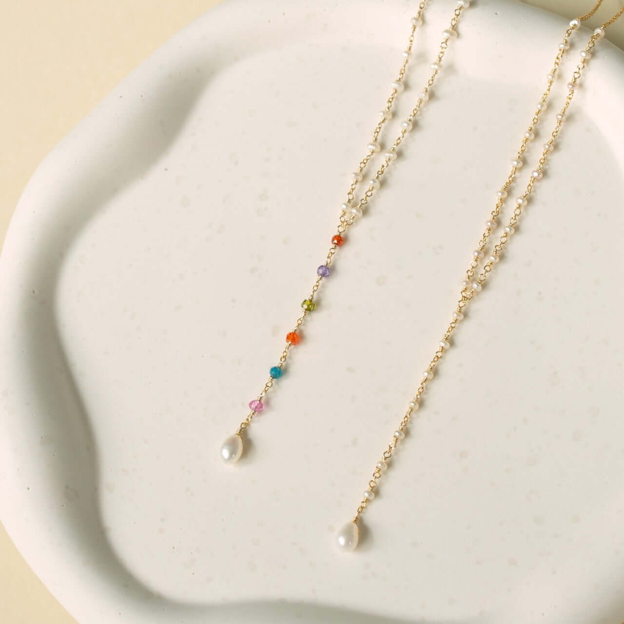 Two charming necklaces: one featuring lustrous freshwater pearls exuding timeless elegance; the other, a playful combination with a pearl pendant and colorful charms—a dynamic pair.
