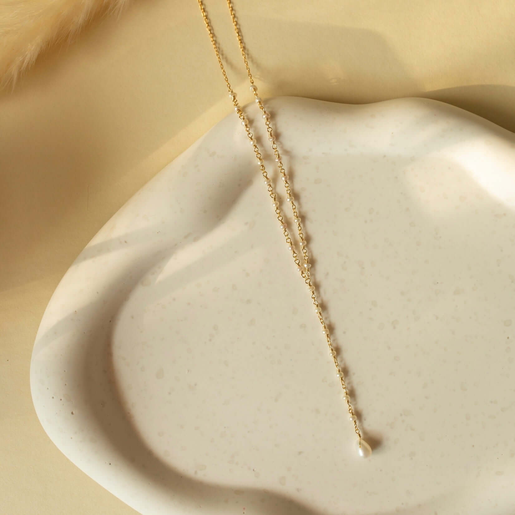 A delicate pearl necklace from The Kensington Collection gracefully rests on a rustic white clay plate