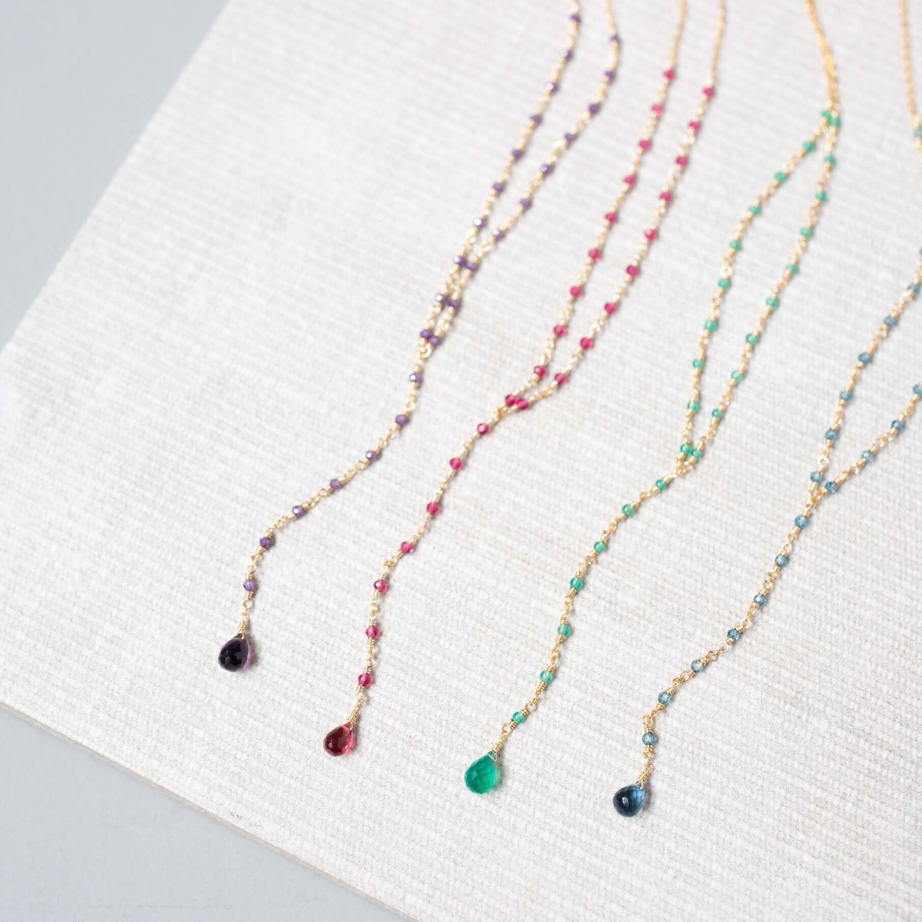 Against a clean white canvas, lolite, amethyst, pink tourmaline quartz, and green onyx necklaces reveal their individual beauty in a scene of pure elegance and simplicity