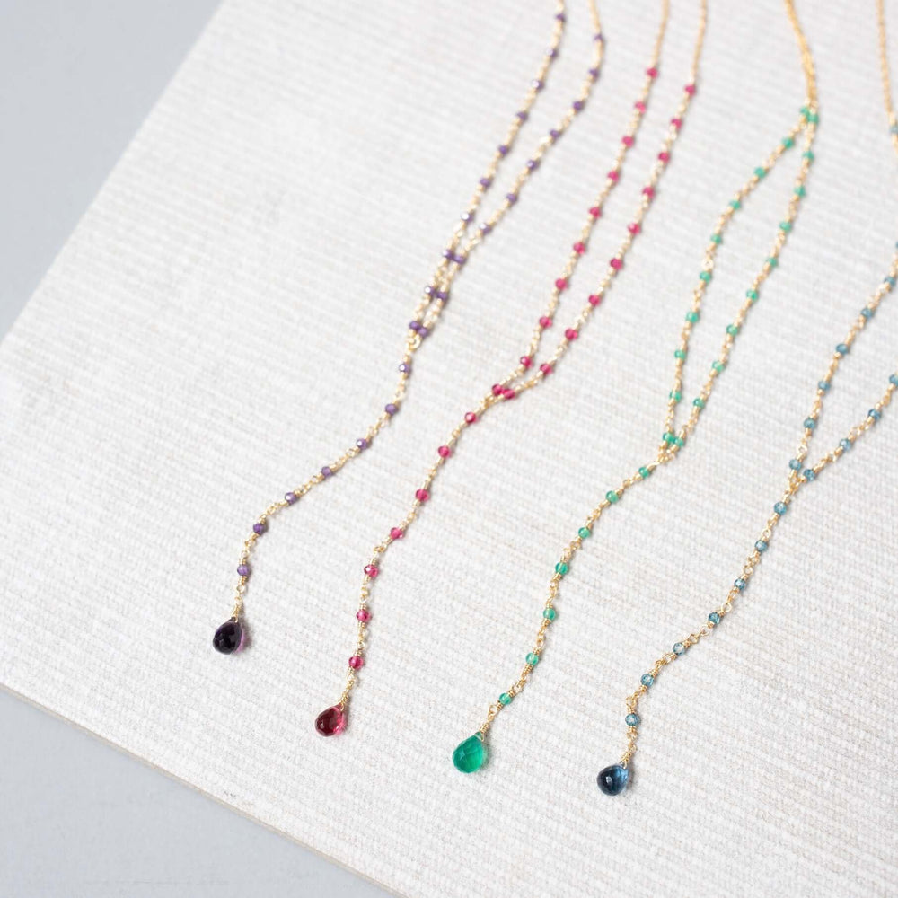 Against a clean white canvas, lolite, amethyst, pink tourmaline quartz, and green onyx necklaces reveal their individual beauty in a scene of pure elegance and simplicity