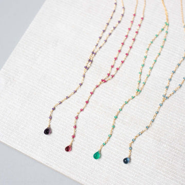 Against a clean white canvas, lolite, amethyst, pink tourmaline quartz, and green onyx necklaces reveal their individual beauty in a scene of pure elegance and simplicity