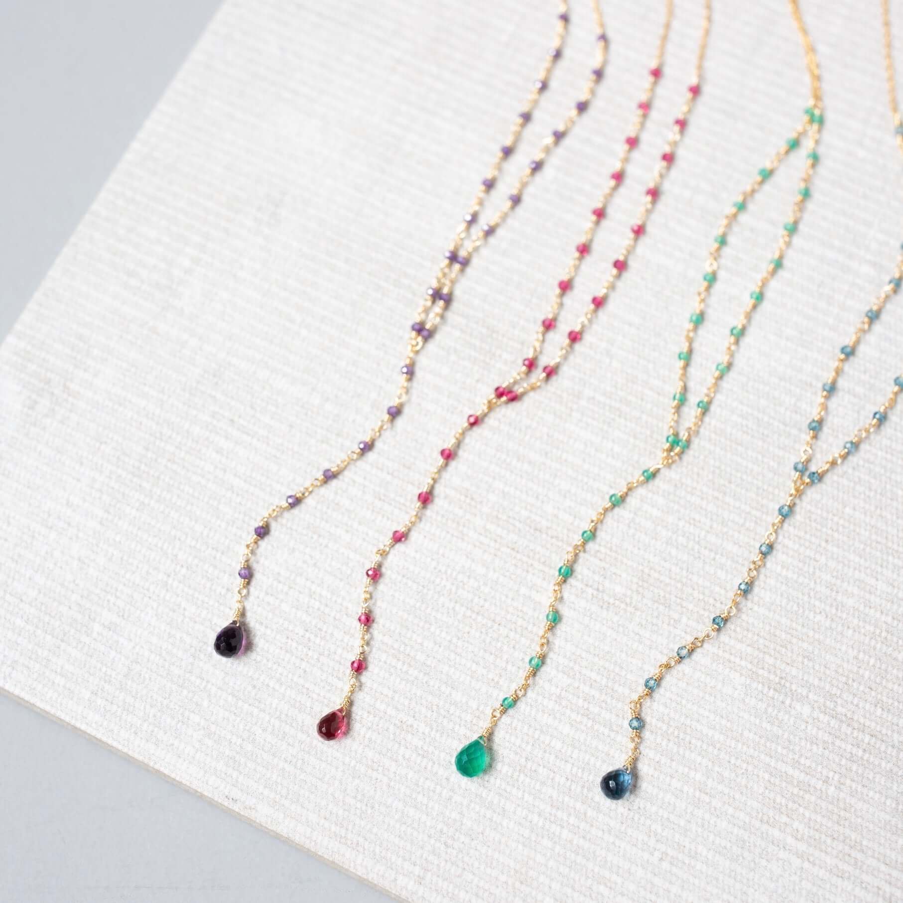 Casually arranged on a white background, necklaces in lolite, amethyst, pink tourmaline quartz, and green onyx bring a natural charm to the scene.