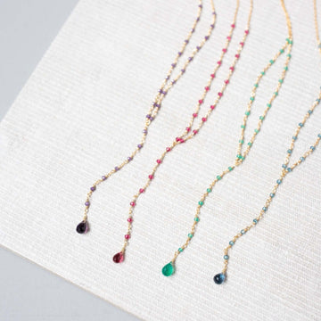 Casually arranged on a white background, necklaces in lolite, amethyst, pink tourmaline quartz, and green onyx bring a natural charm to the scene.