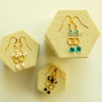 Three pairs of earrings in hexagonal jewelry displays on a light yellow background