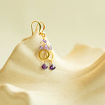 Gold earrings with amethyst gemstones on a beige background.