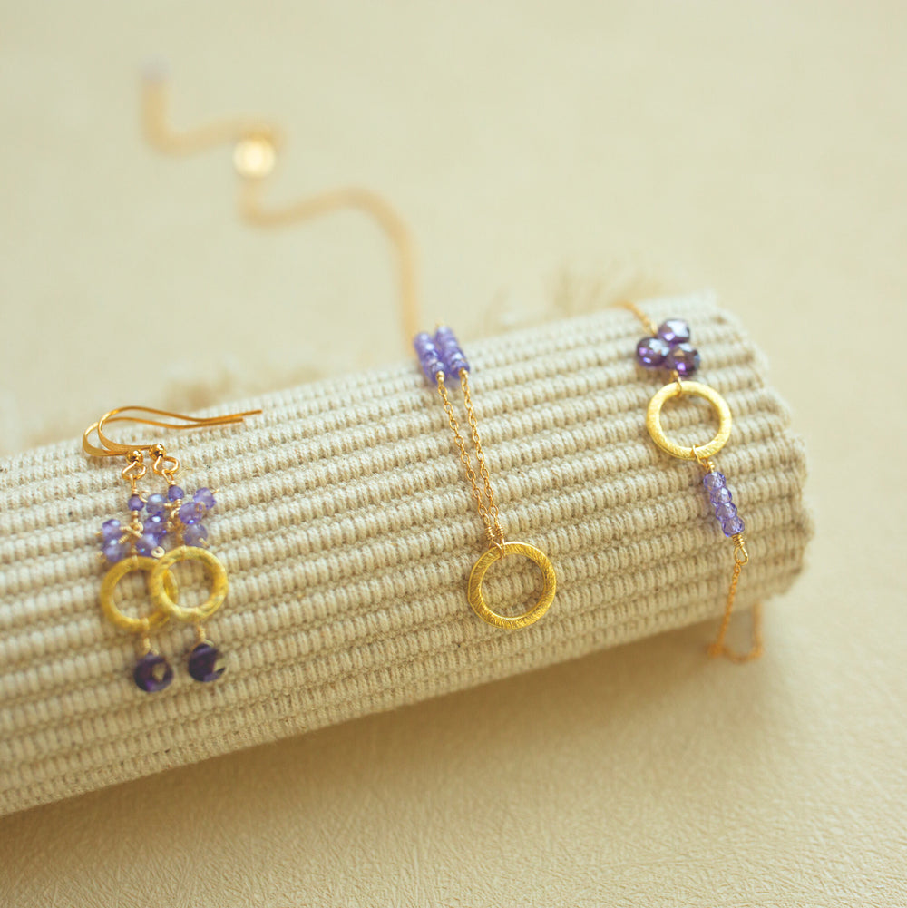Gold and amethyst beaded jewelry on a textured beige surface