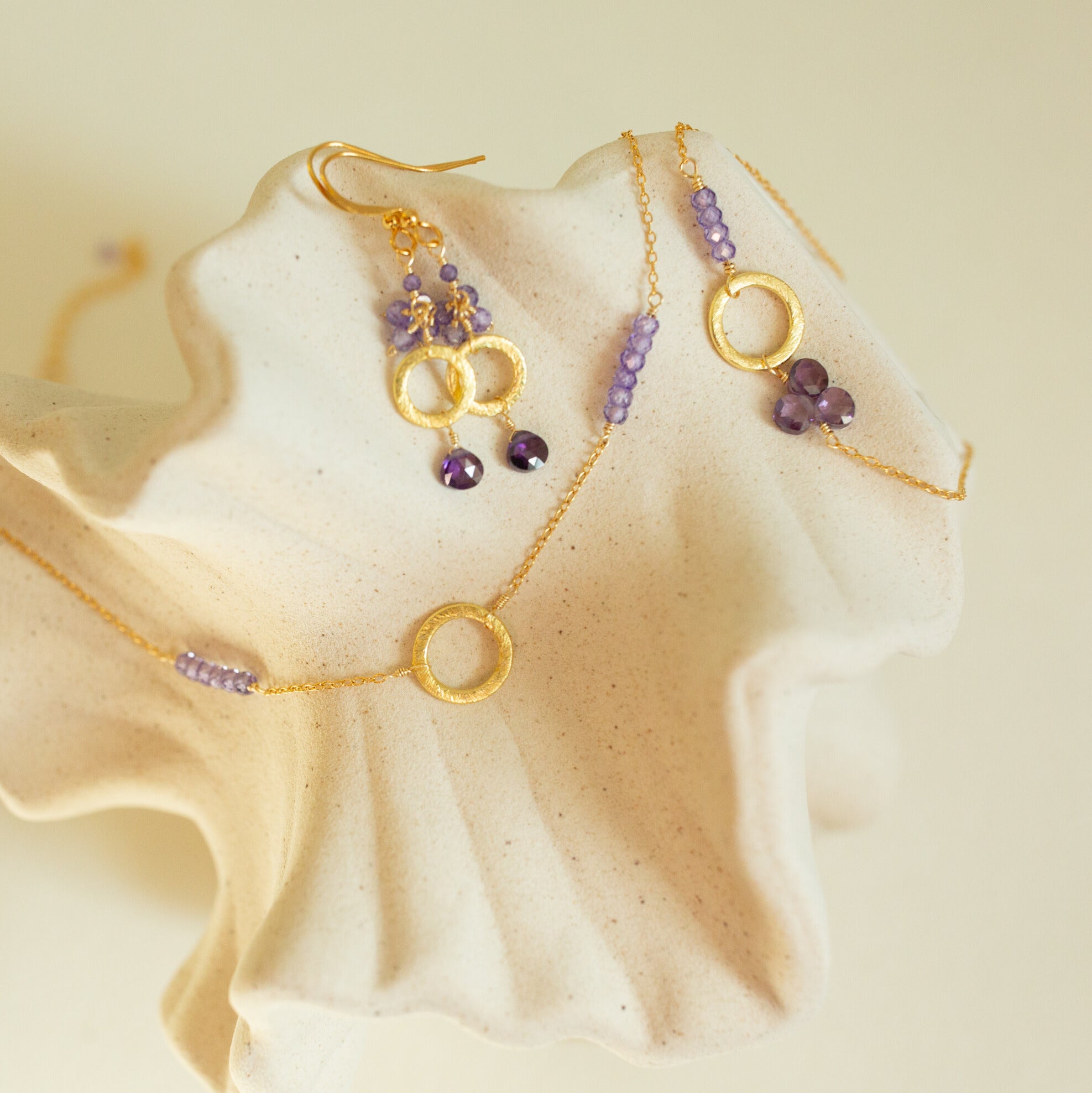 Gold necklace, earrings and bracelet with amethyst beads on a beige background