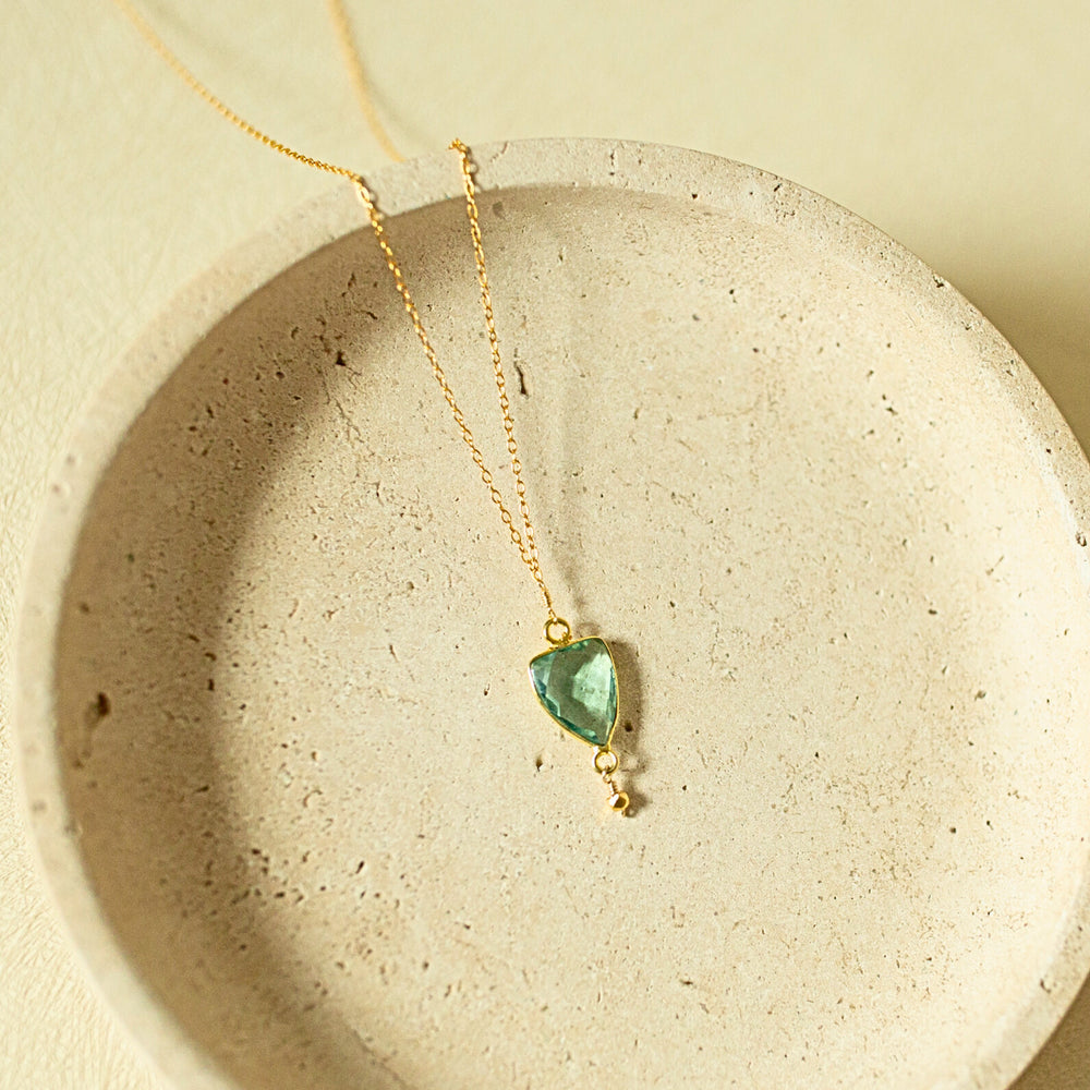 Gold necklace with a green pendant on a beige stone surface